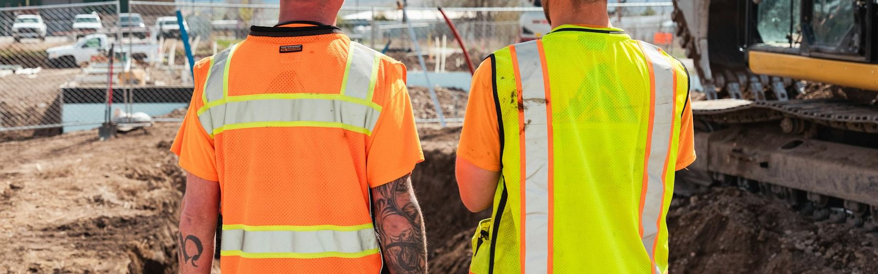 Two site personnel in high-visibility vests beside a working excavator