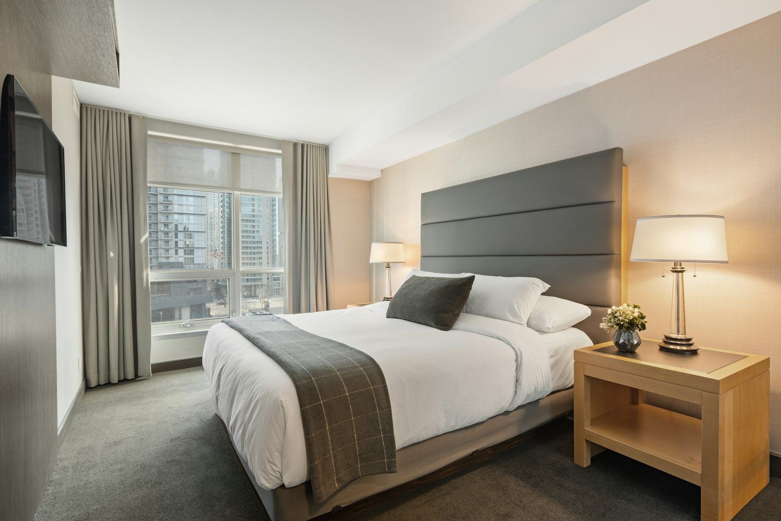 Freshly made hotel room with crisp linen, bedside lamps and a city view