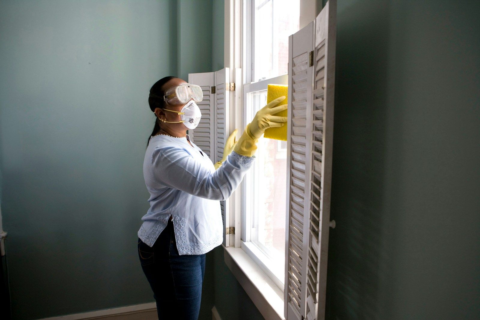 Housekeeping staff member in gloves and mask cleaning interior glazing